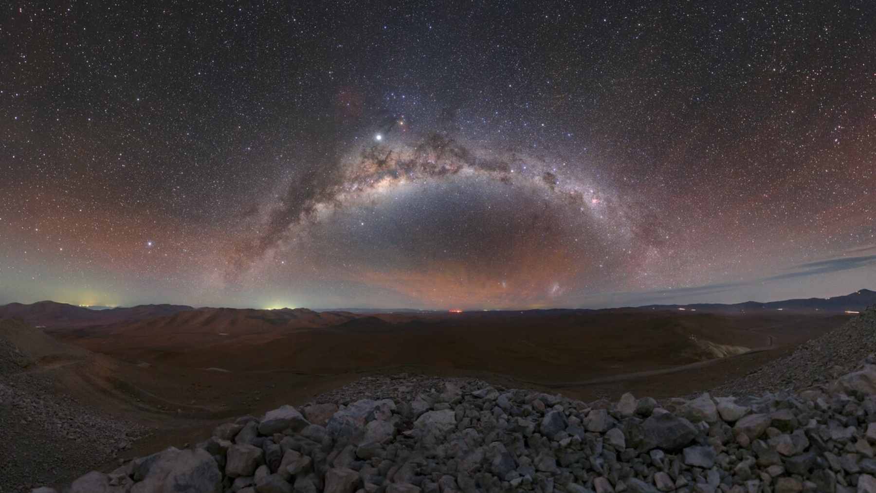 A long-exposure photograph of the Milky Way stretching over the domes of the Very Large Telescope at Paranal Observatory in the Atacama Desert.