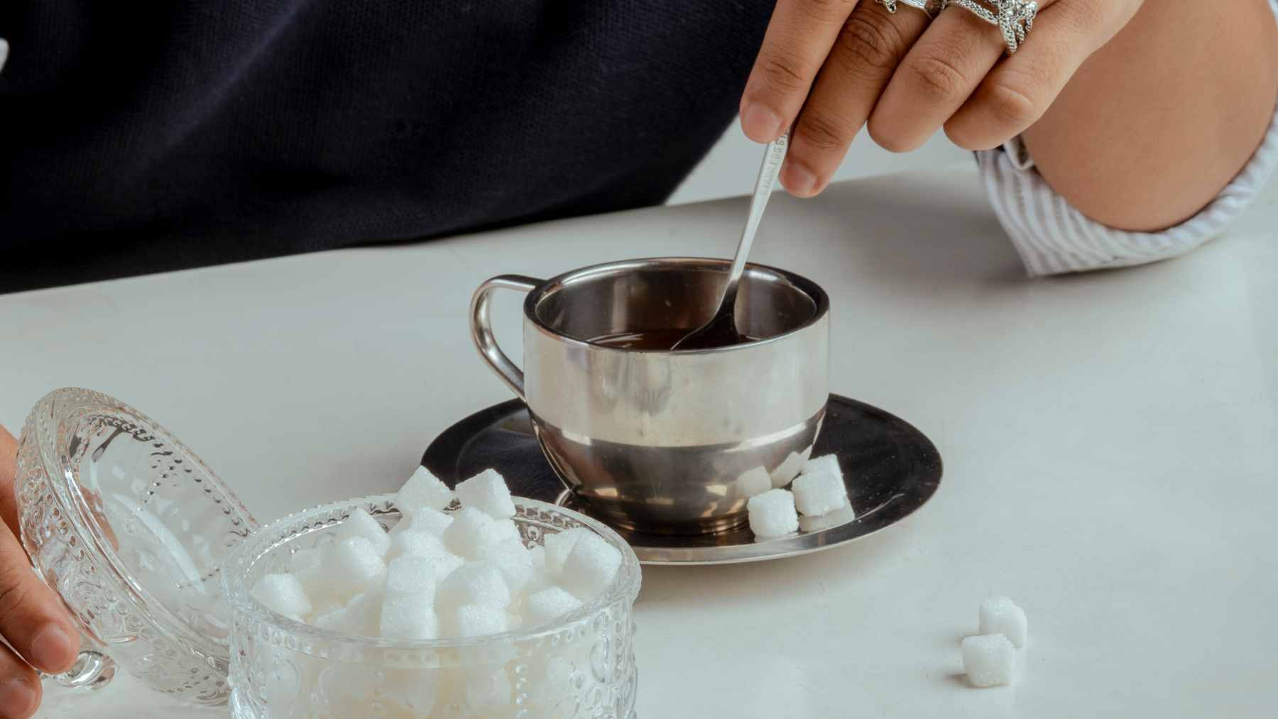 A close-up of an iced diet soda glass next to a bowl of artificial sweetener packets on a wooden table.