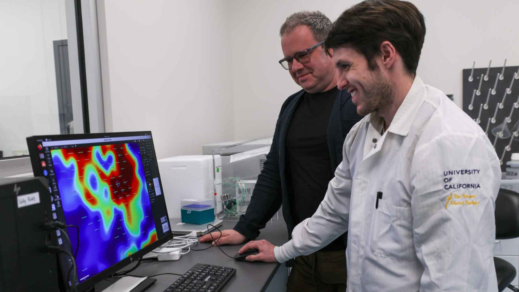 Two researchers at the University of California, Santa Cruz look at a computer monitor displaying a colorful heatmap of neural activity from a brain organoid.