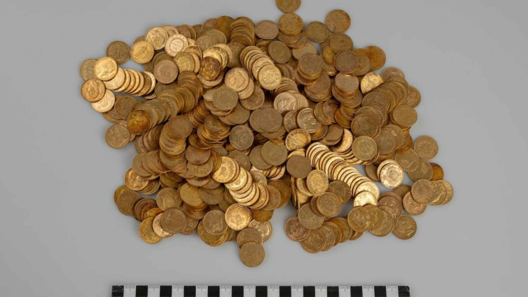 Two hikers spot a “strange” wall and end up finding gold coins dating from 1808 to 1915… and the hiding place looks like an “emergency plan” 1 Pile of gold coins from a Czech treasure hoard found by hikers, shown with a measuring scale.