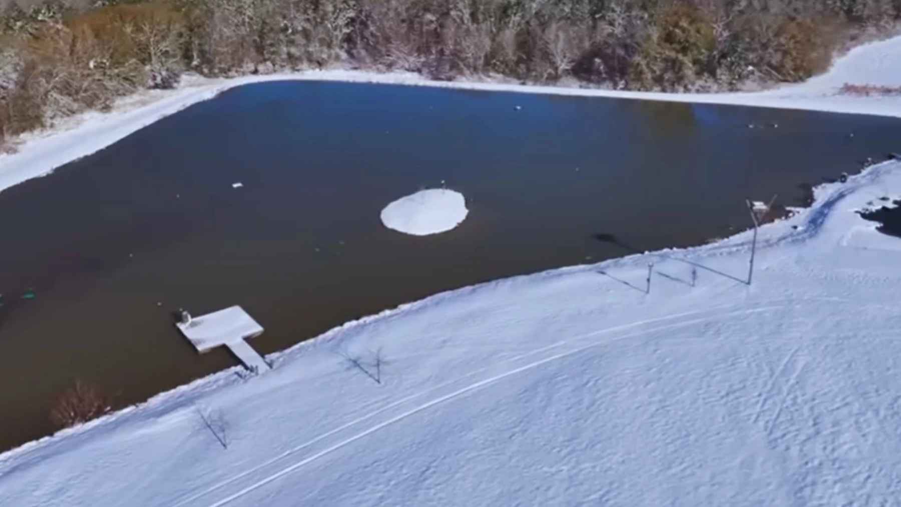 Aerial view of a five-acre artificial lake surrounded by snow and forest habitat attracting wildlife