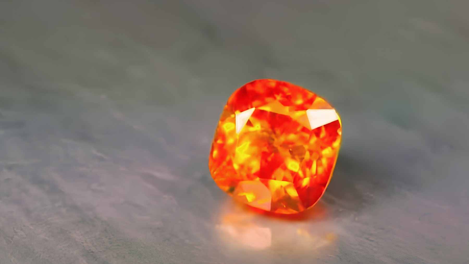 A close-up view of a tiny, reddish-orange kyawthuite crystal, the only confirmed natural specimen of this mineral species in existence.