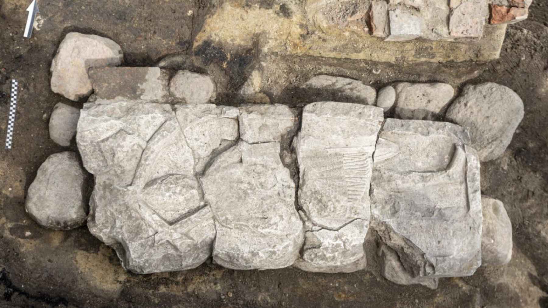 Cracked medieval limestone tomb slab showing a carved knight at an archaeological site in Gdańsk, Poland.