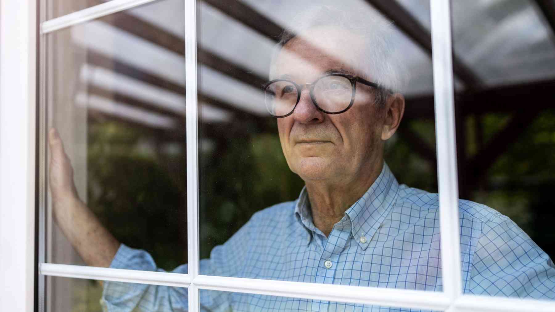 Older man looking through a window, reflecting loneliness and the emotional weight of lacking close friends after 60