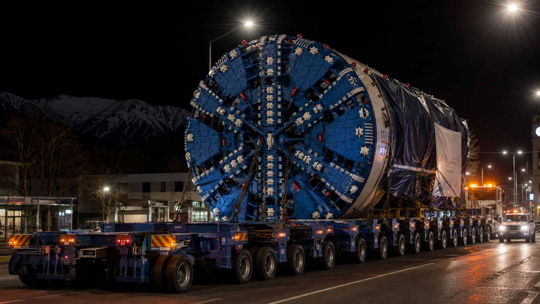 A massive center cutterhead section for a tunnel boring machine being transported on a 152-wheel specialized trailer through city streets.