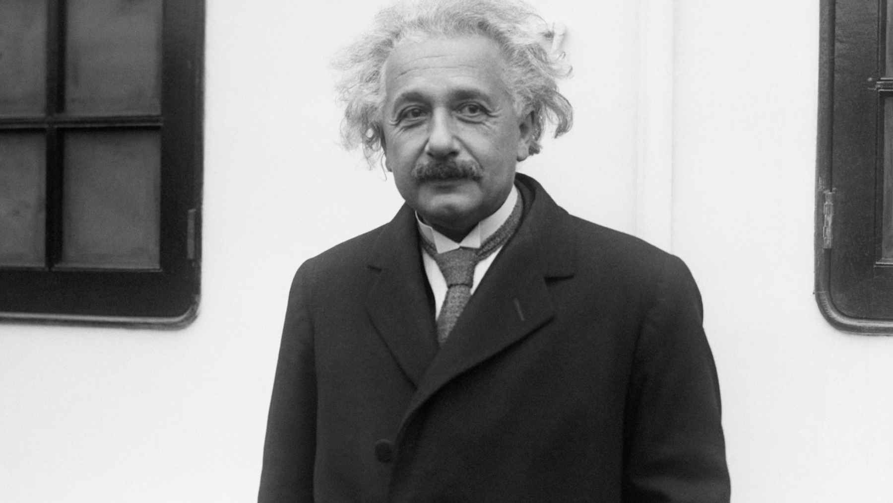 Albert Einstein standing in a dark coat, linked to his famous quote about becoming a person of value.