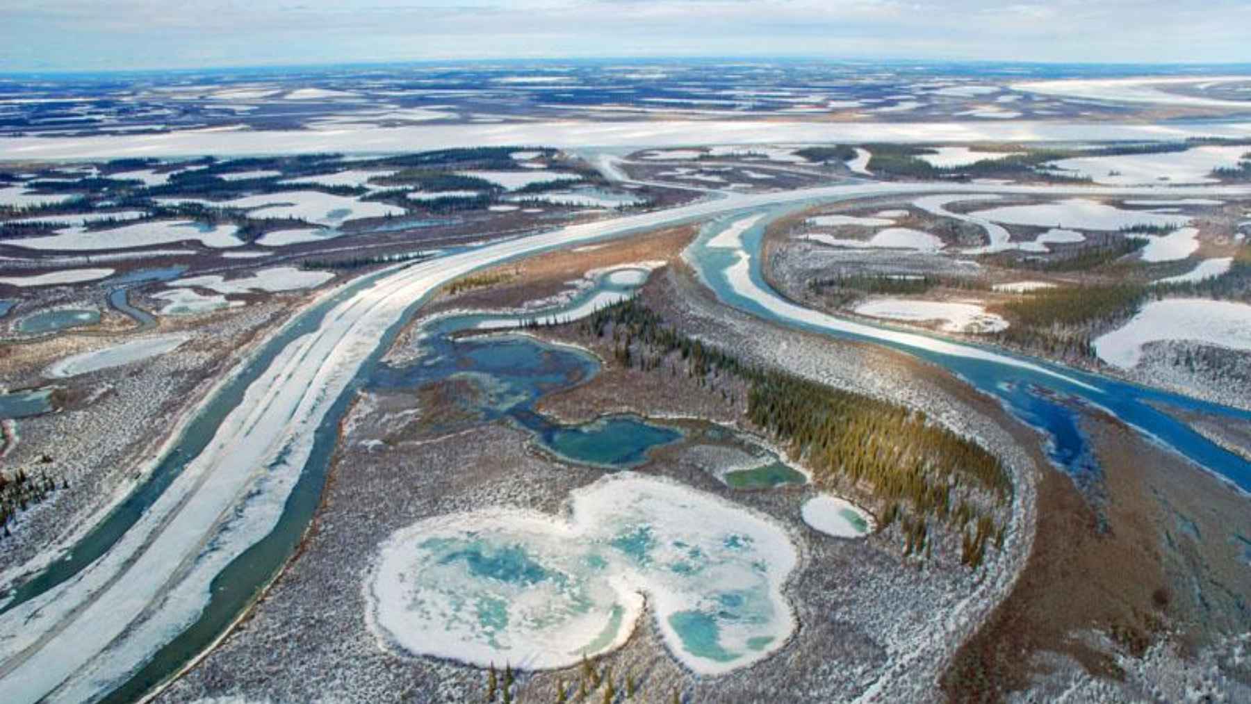 Arctic river delta with thawing permafrost, water channels, and thermokarst lakes forming as frozen ground melts.