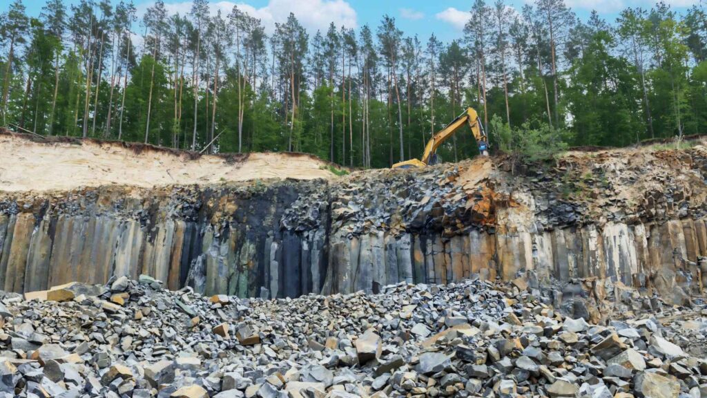 Basalt quarry with exposed volcanic rock layers and excavator, showing material proposed as a low-carbon alternative for cement production.