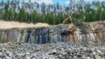 Basalt quarry with exposed volcanic rock layers and excavator, showing material proposed as a low-carbon alternative for cement production.