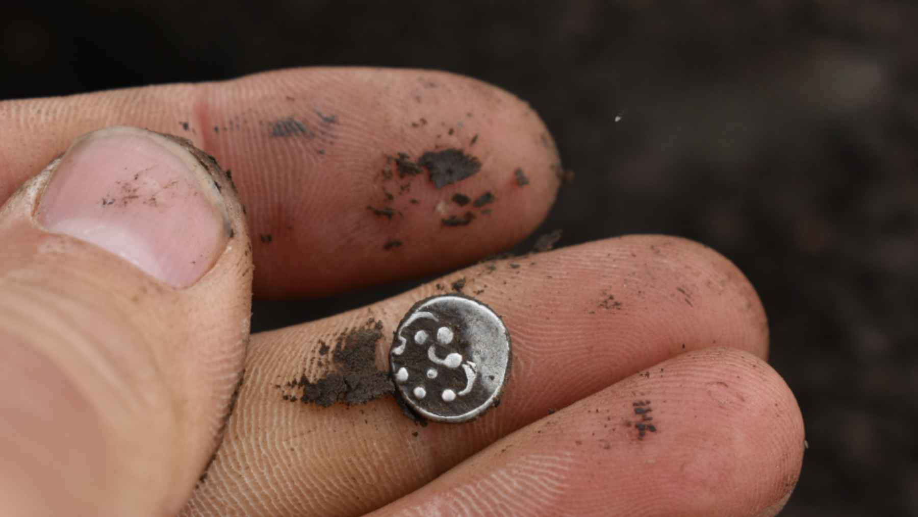 A small Celtic silver coin resting on muddy fingers during an excavation near Hradec Králové in Bohemia.