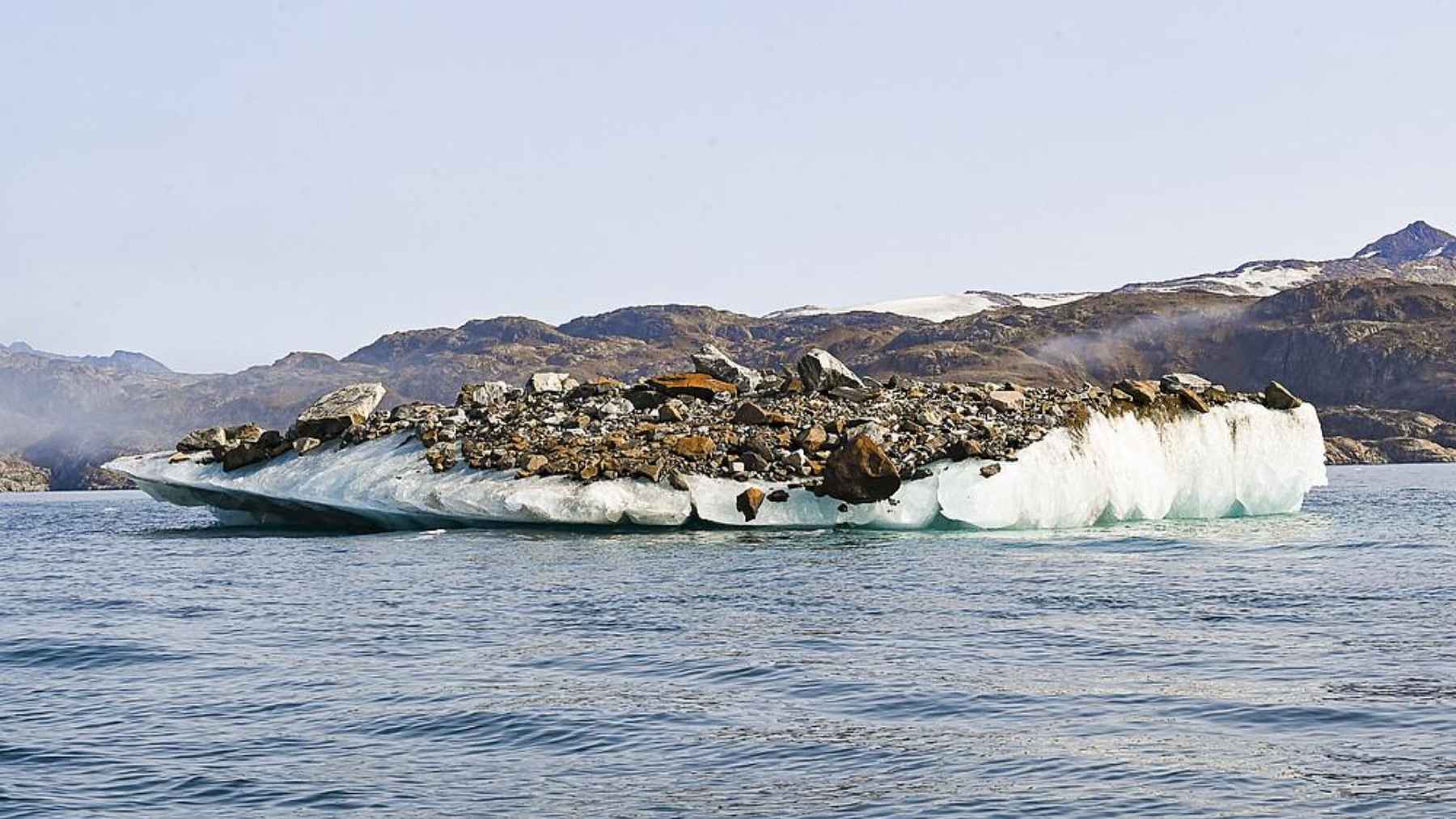Iceberg carrying rocks and sediment floating in Arctic waters.