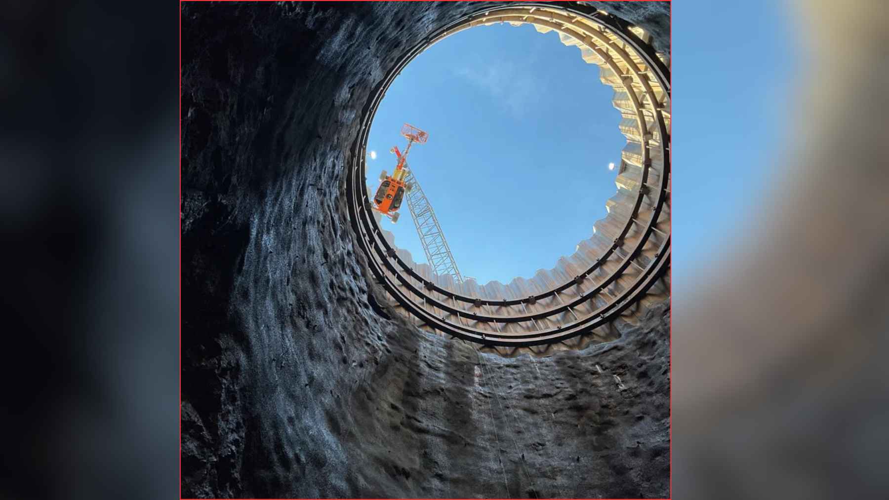Workers prepare a circular drill-and-blast pattern at the base of a deep shaft for tunnel excavation.