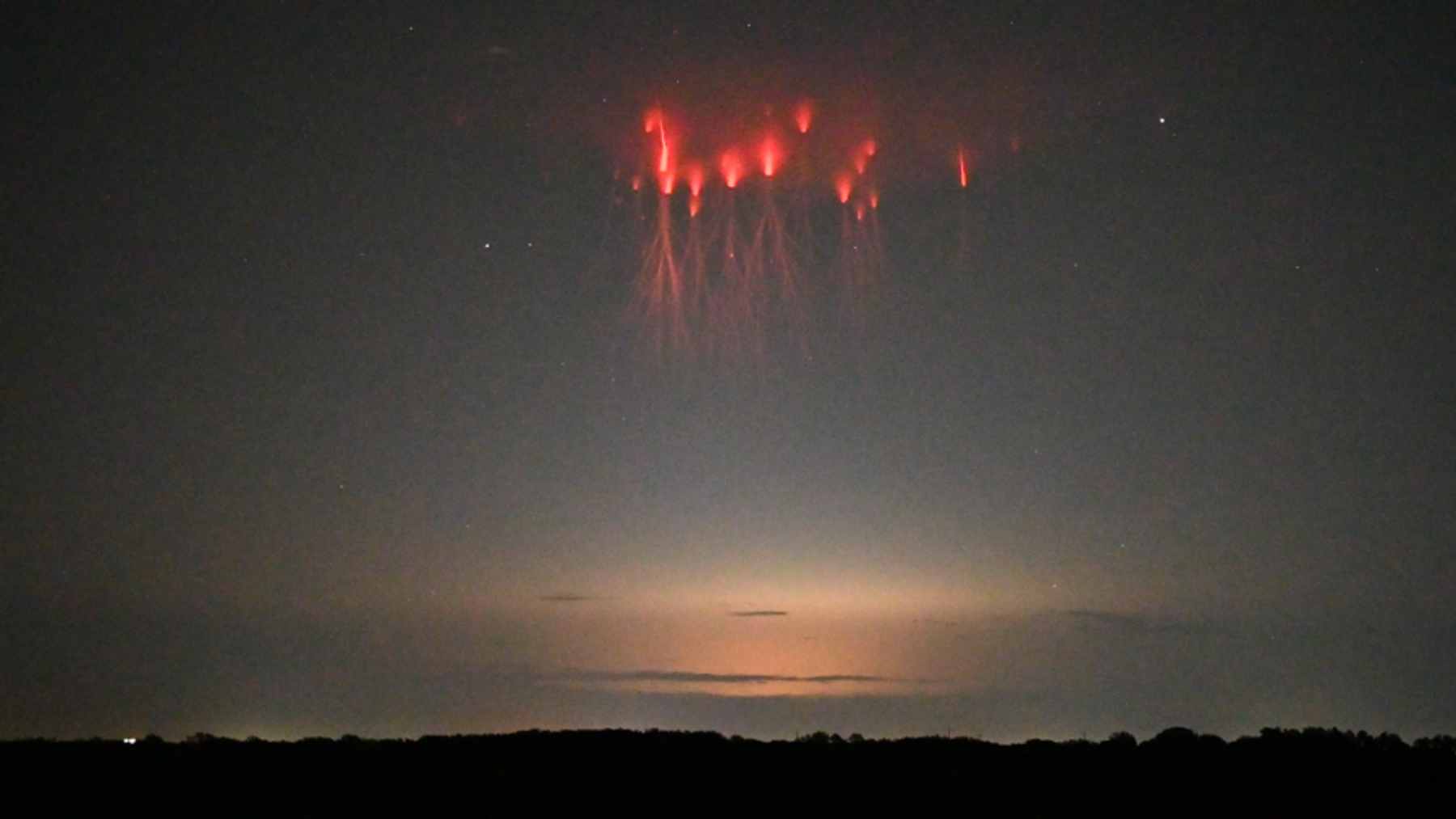 A view from the International Space Station showing a vibrant red gigantic jet lightning event discharging above a thunderstorm.