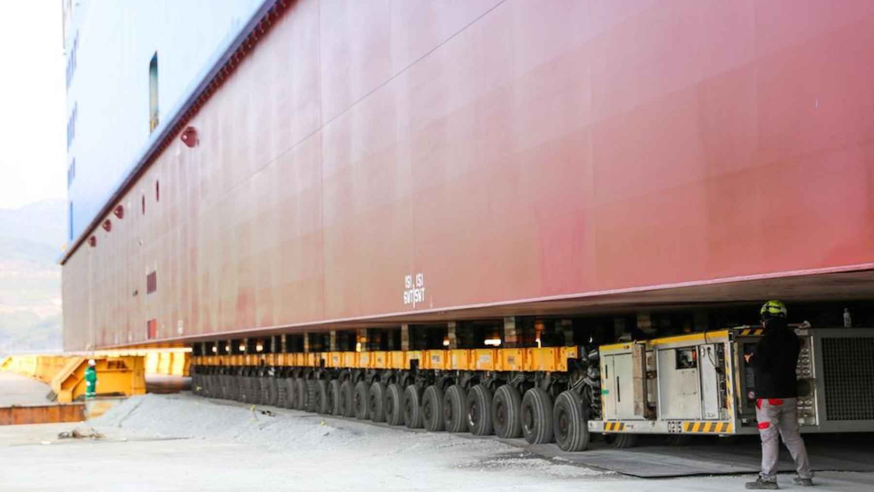 The heaviest load ever hauled by a trailer was a roughly 16,300-ton naval block, and the 324-axle transport looks like industrial choreography designed not to crack the ground 1 Self-propelled modular transporter with hundreds of wheels moving a massive ship block in a shipyard.