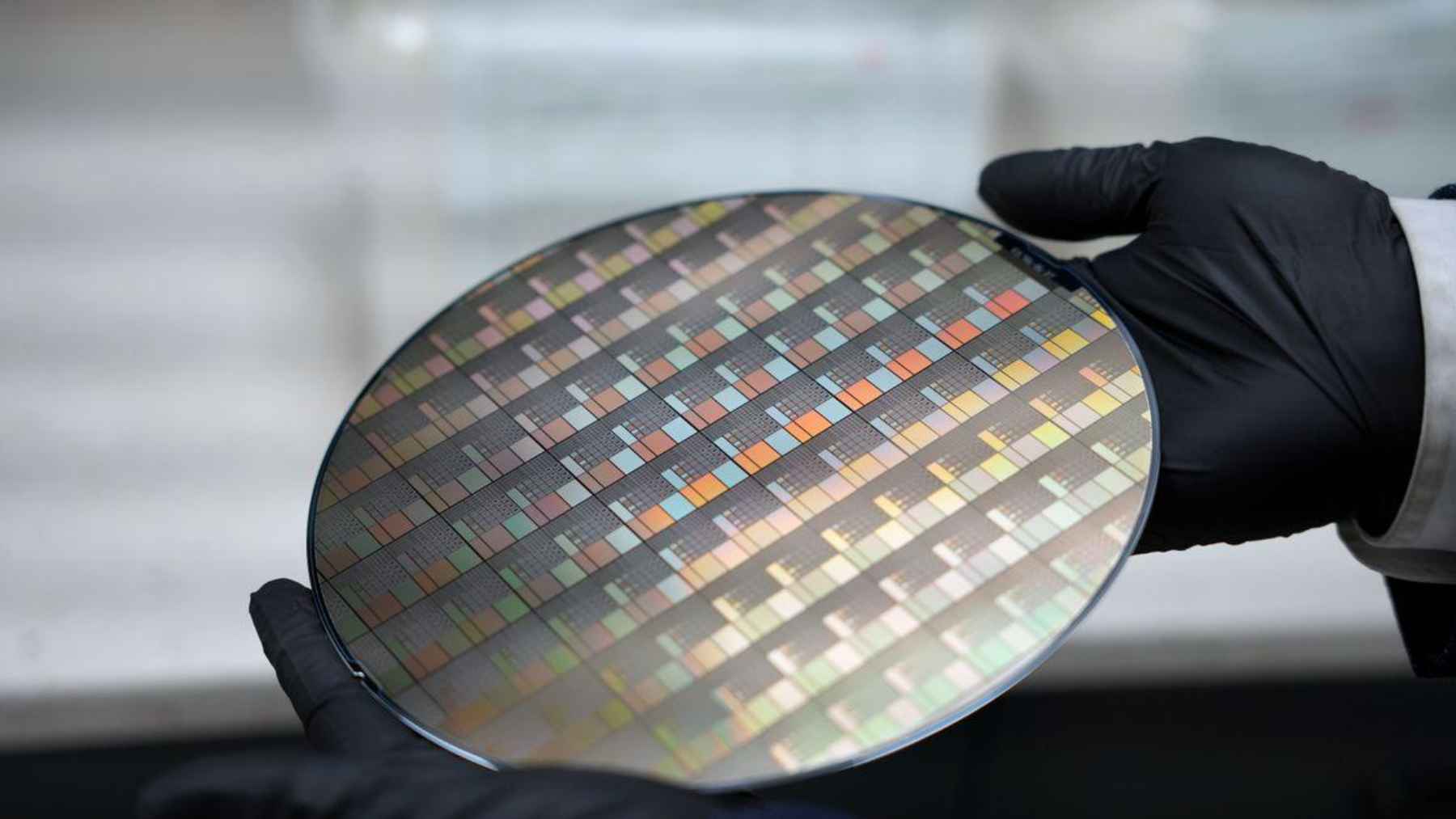 Gloved hands holding a semiconductor wafer linked to research on safer plasma processing for future ultrathin chips.