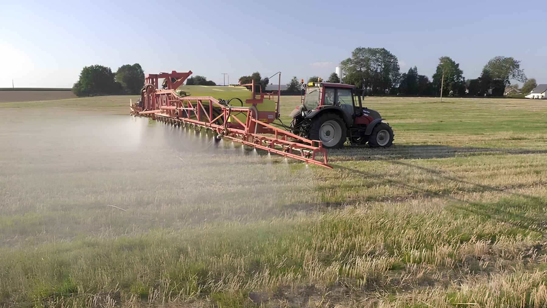 Tractor spraying herbicide across farmland during crop treatment