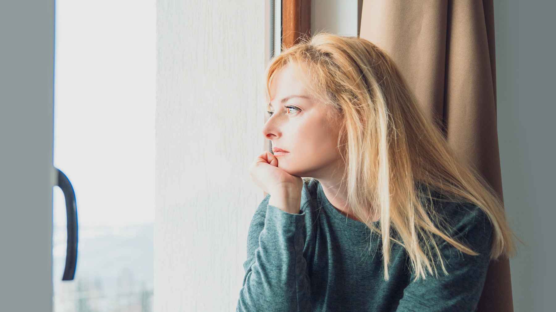 Woman looking out a window, reflecting on emotional distance, guarded relationships, and childhood harm.