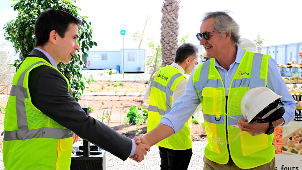 Acciona executives in safety vests shake hands at the Casablanca desalination plant site after securing project financing.