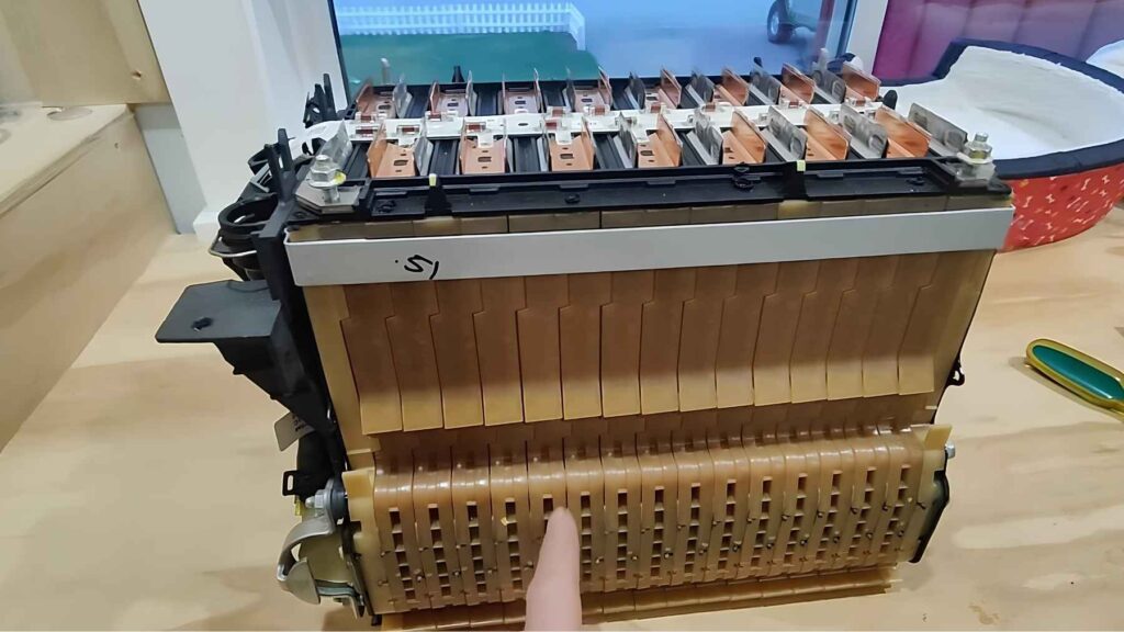EV battery module on a workbench, showing individual cell stacks and copper busbars during a teardown inspection.