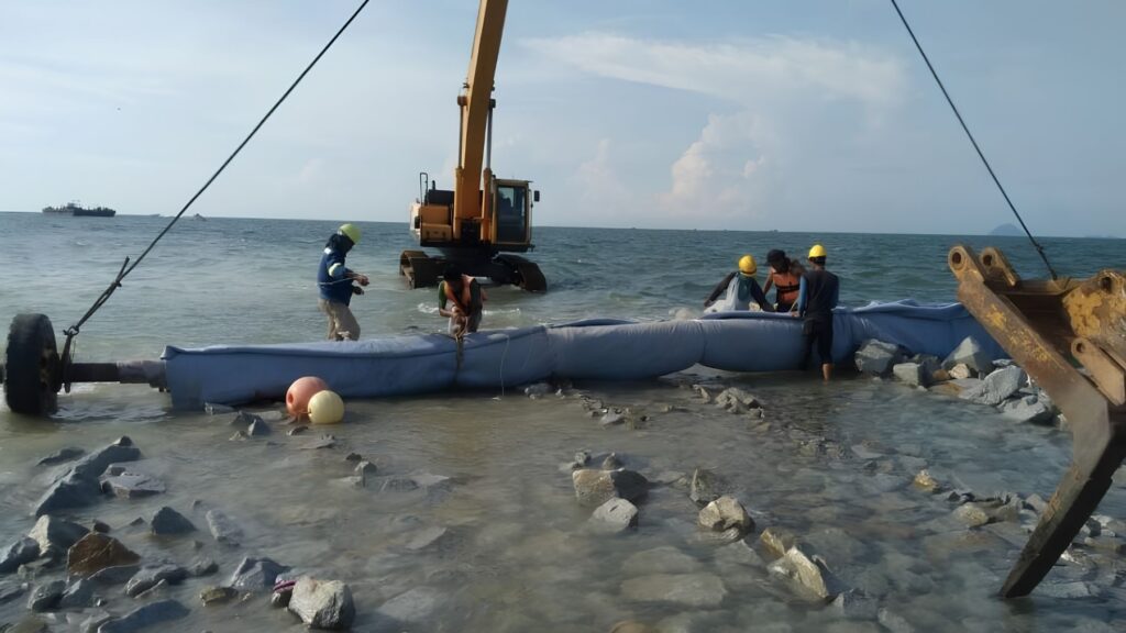 Workers install giant sand-filled geotubes along the coast of Poonthura, India, as part of a submerged breakwater project.
