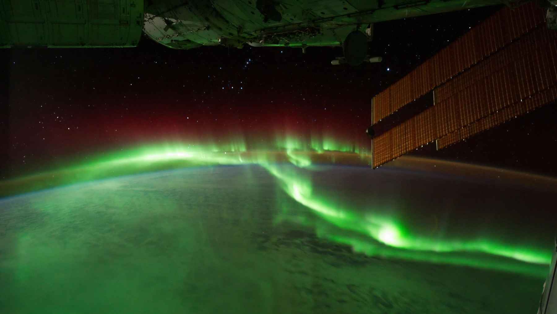 Green aurora australis glowing above Earth as the International Space Station passes over the planet at night.