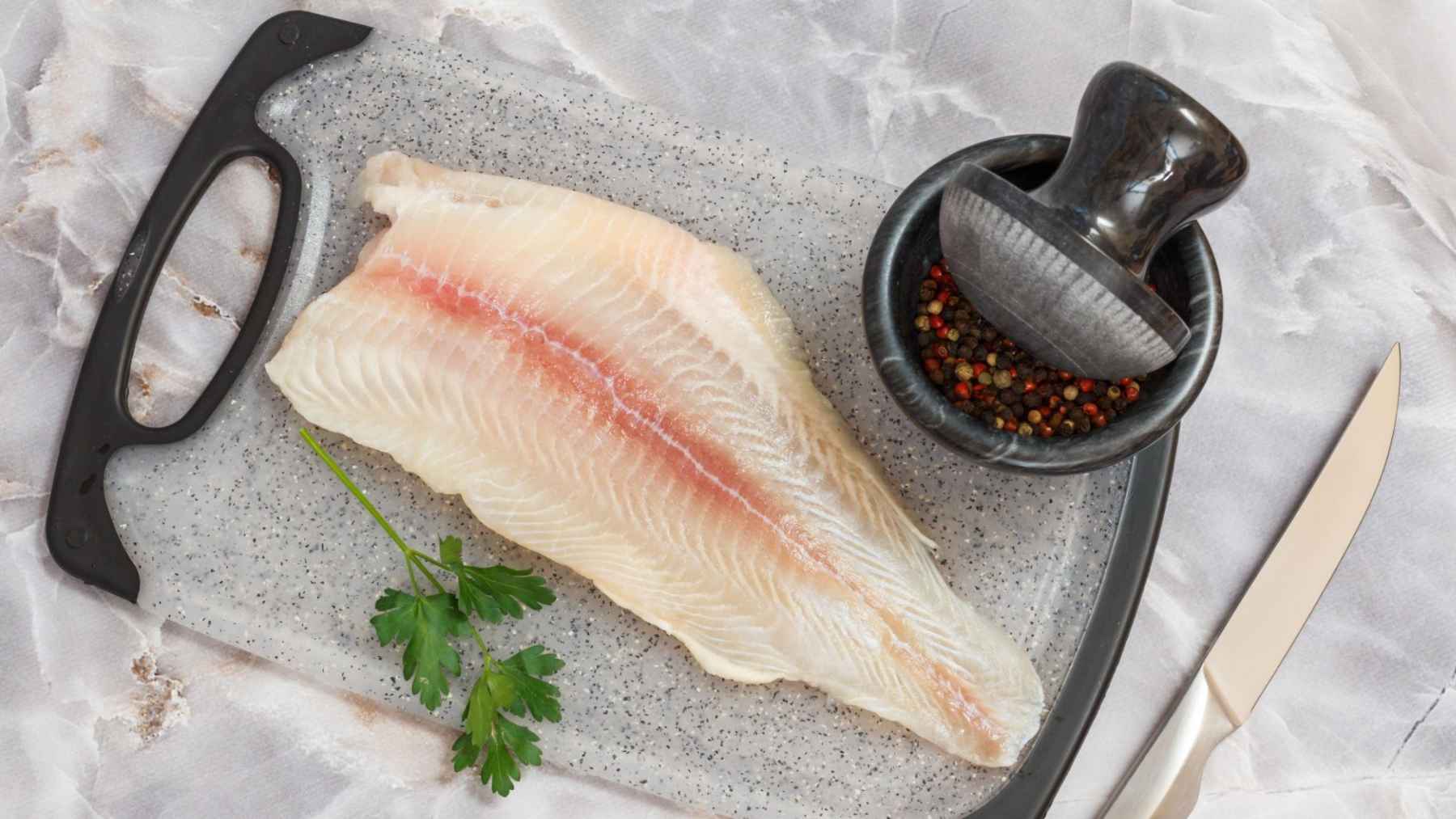 Raw pangasius white fish fillet on a cutting board, commonly sold as an affordable frozen seafood product.