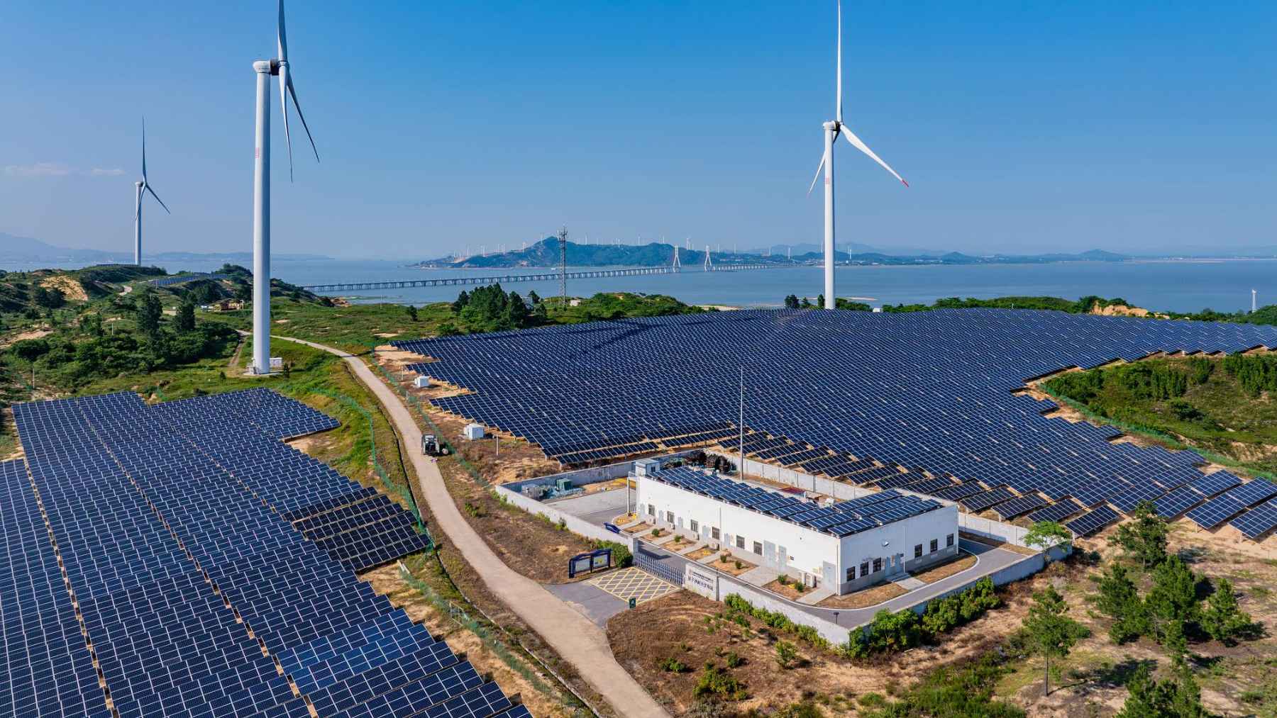The green economy has just surpassed $10 trillion and would already be the world's third-largest industry if it were counted as a separate sector 1 Large solar farm and wind turbines generating renewable energy near a coastal landscape.