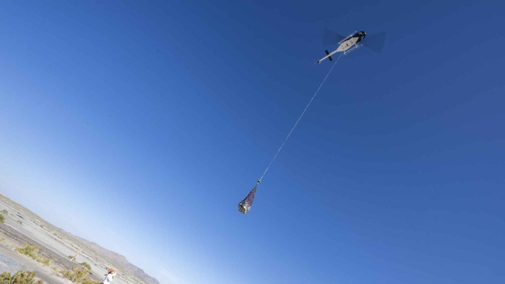 Helicopter lifting a space sample return capsule in a desert recovery operation after landing