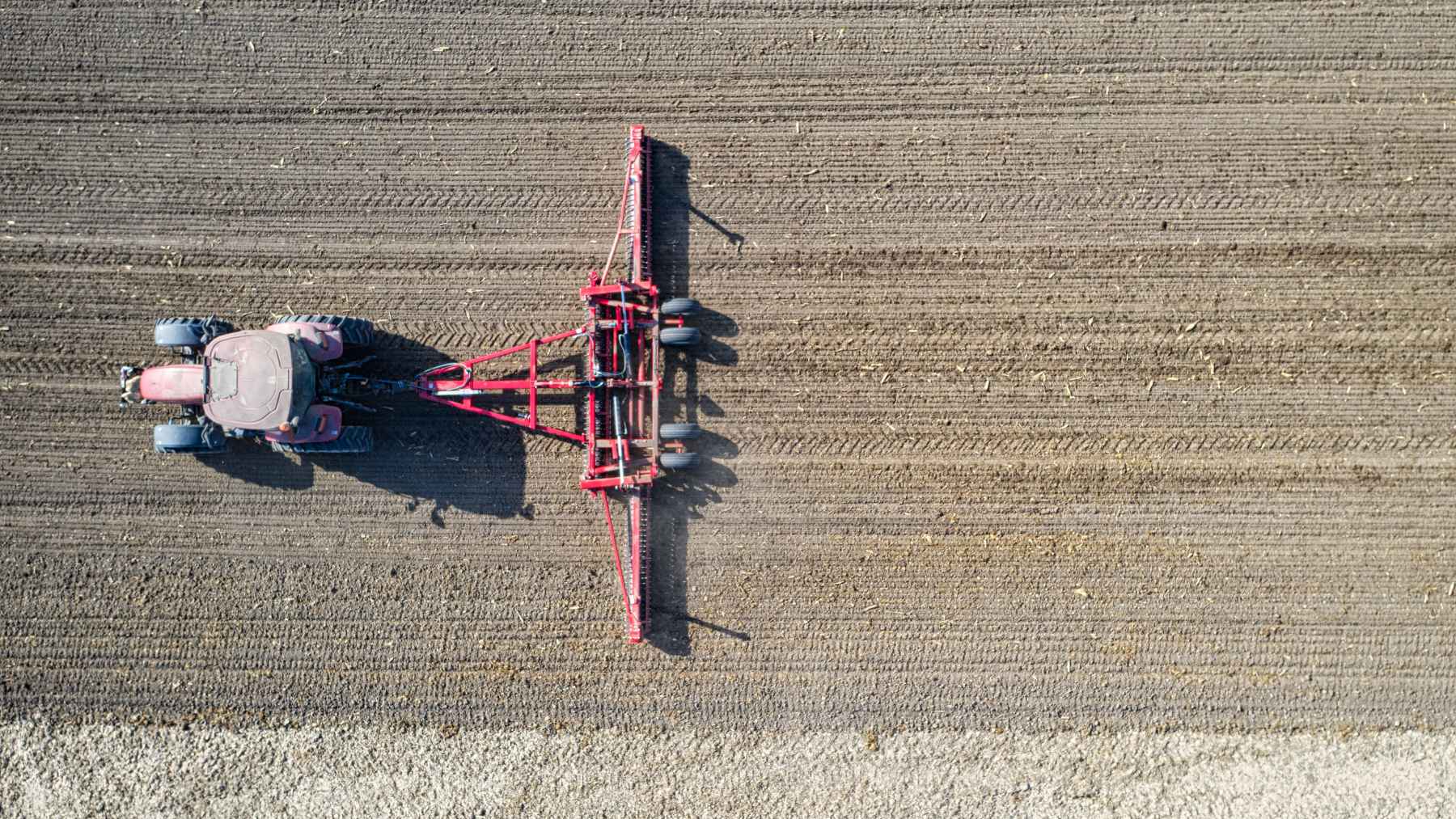 A Russian university has just unveiled a tractor attachment that injects cooled exhaust gases directly into the soil—a highly unusual idea that promises to benefit crops but requires extensive testing under real-world conditions 1 Aerial view of a tractor pulling a field implement across cultivated soil, illustrating a carbon farming and soil treatment concept.