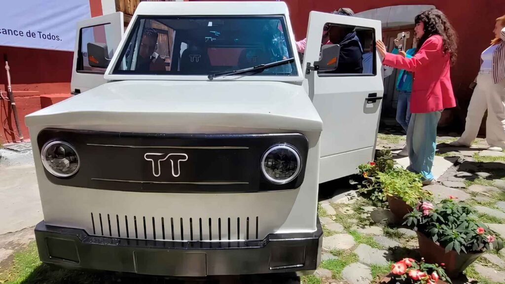 TT Automotriz TT01 prototype displayed in a Tlaxcala courtyard with its doors open as attendees inspect the solar-assisted EV.