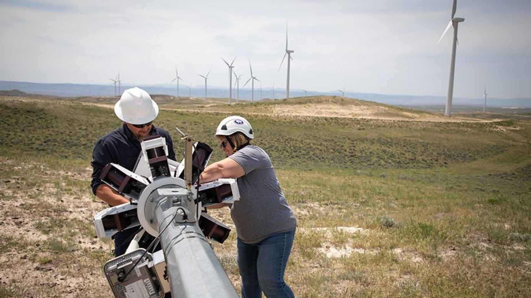 Technicians work on an IdentiFlight camera system at a wind farm in Wyoming, with wind turbines visible in the background.