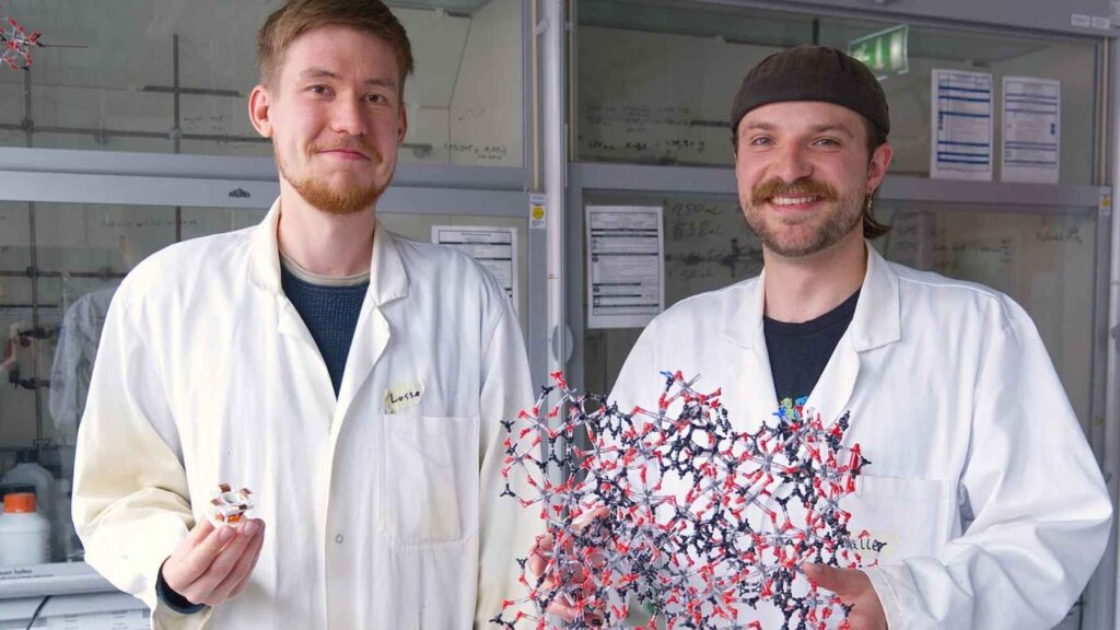 Researchers Lasse Wegner and Kalle Mertin presenting a prototype atmospheric water harvesting cell and a model of the porous CAU-10-H metal-organic framework.