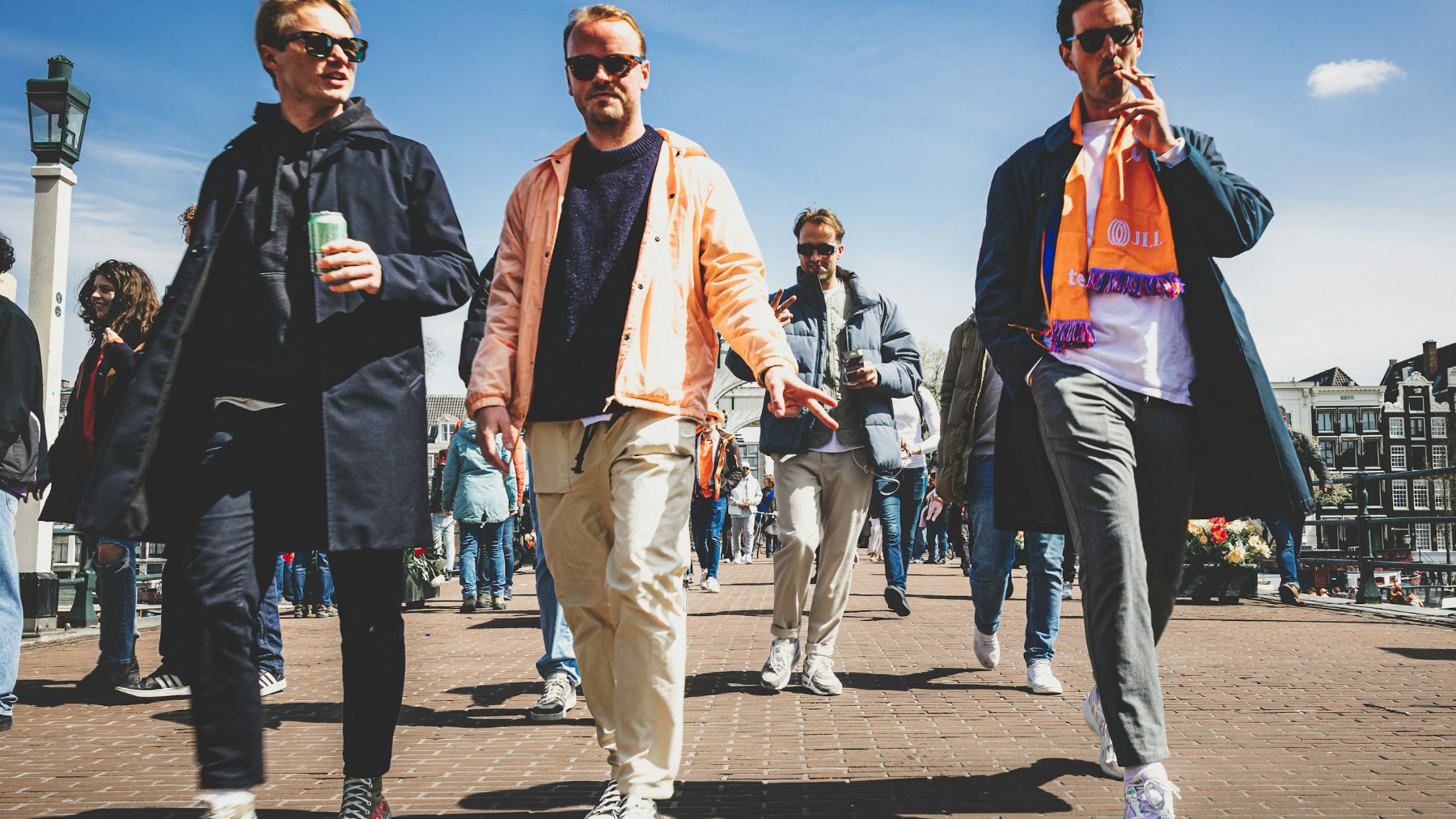 Three tall men walking together on a street in Amsterdam with Dutch canal houses behind them