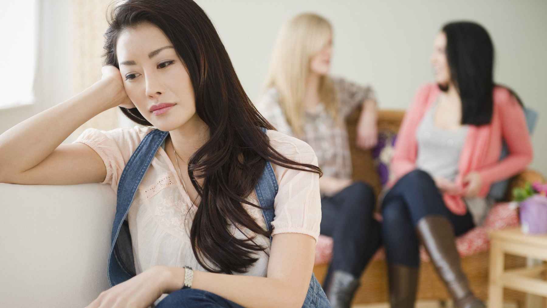 Woman sitting apart from friends during a social gathering.