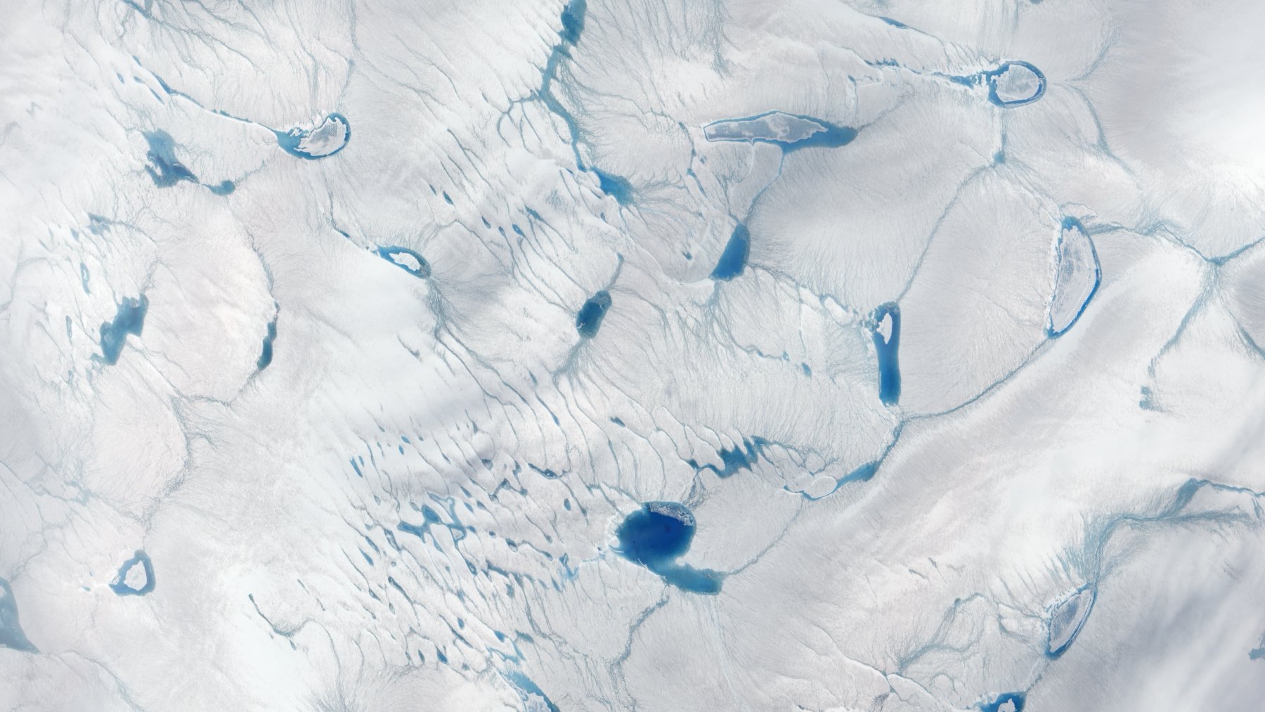 Meltwater ponds spreading across the surface of the Greenland ice sheet