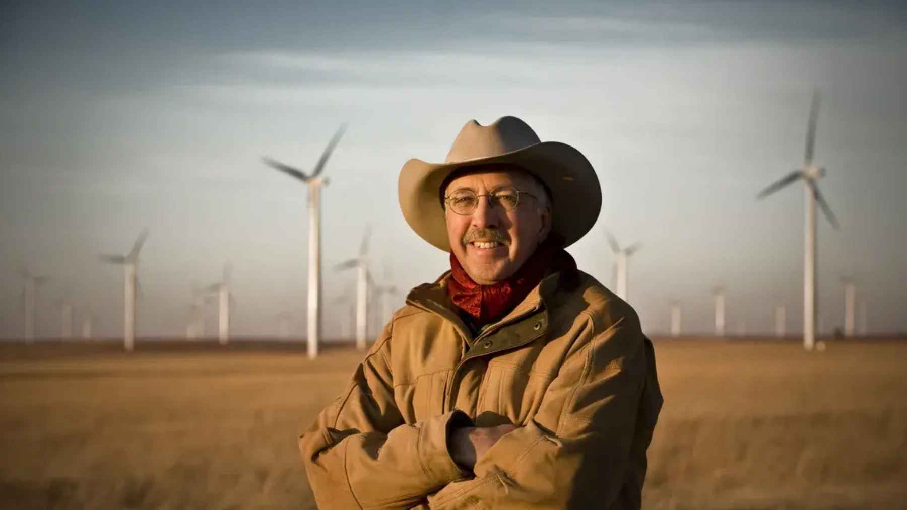 Kansas rancher Pete Ferrell standing in a field with wind turbines behind him