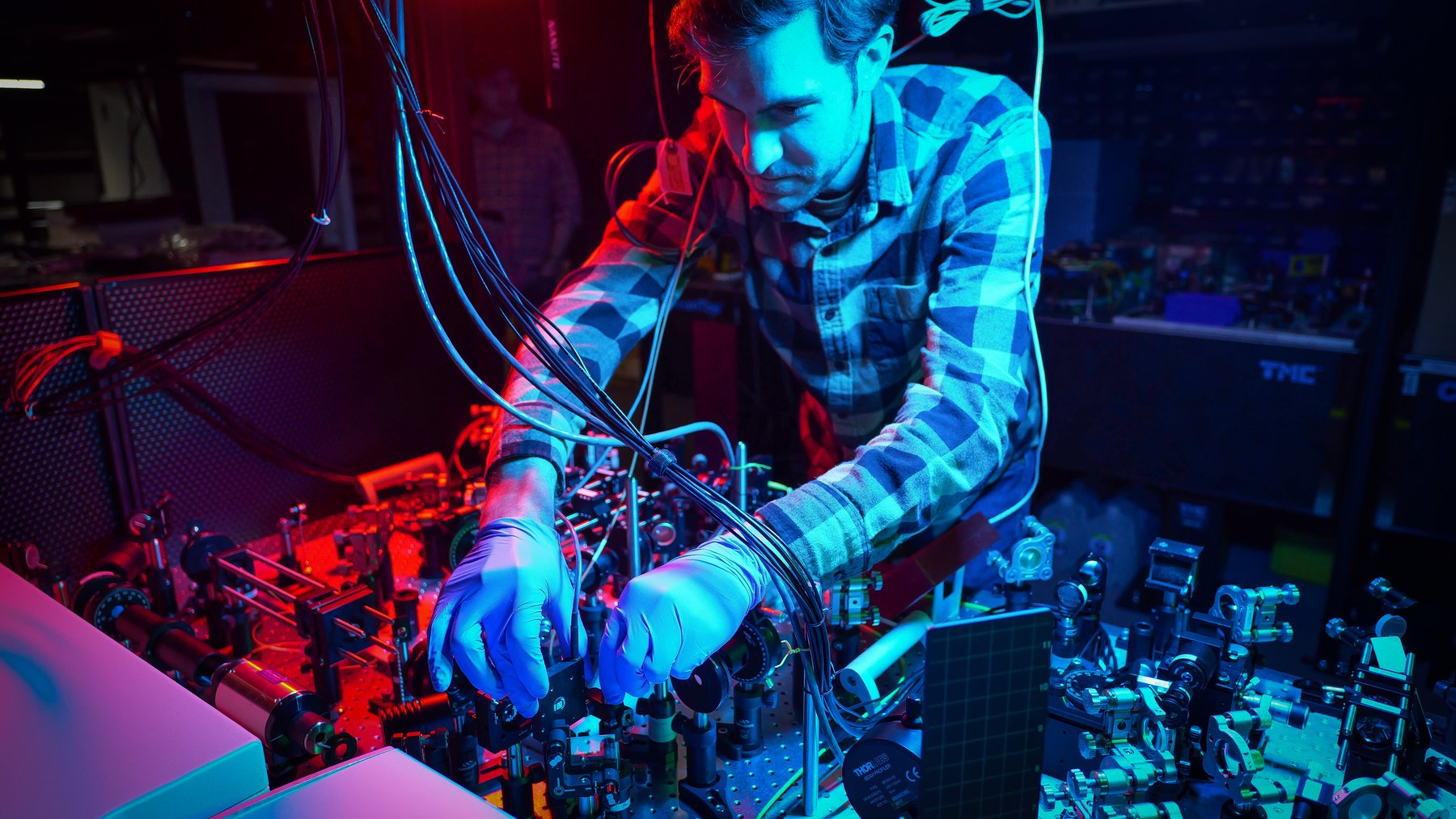 Researcher adjusting optical components on a laser table in a quantum physics laboratory lit in red and blue
