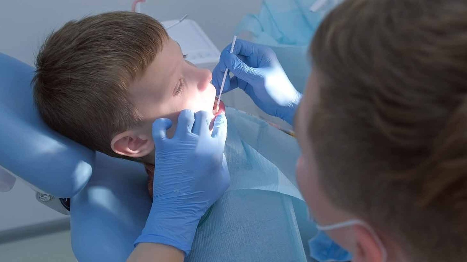 Dentist applying a liquid treatment to a young child's teeth with a small brush