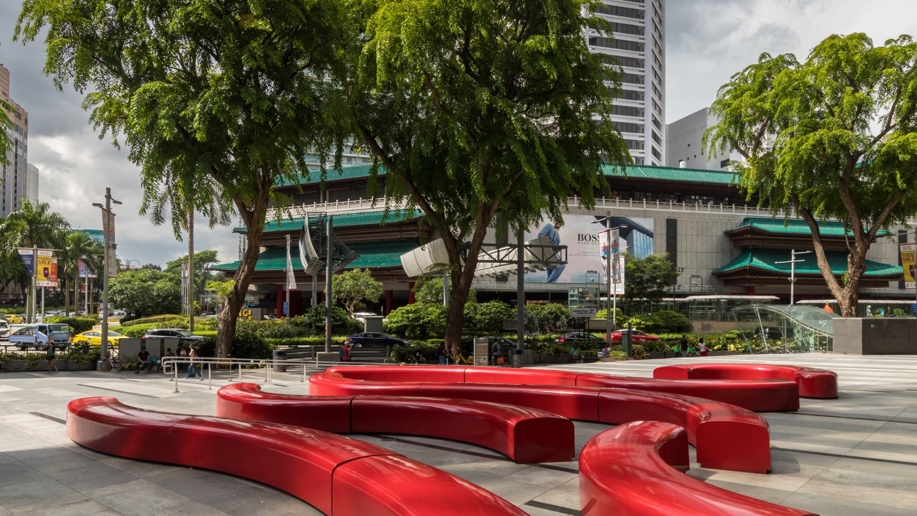 Angsana trees shading red curved benches on a Singapore street