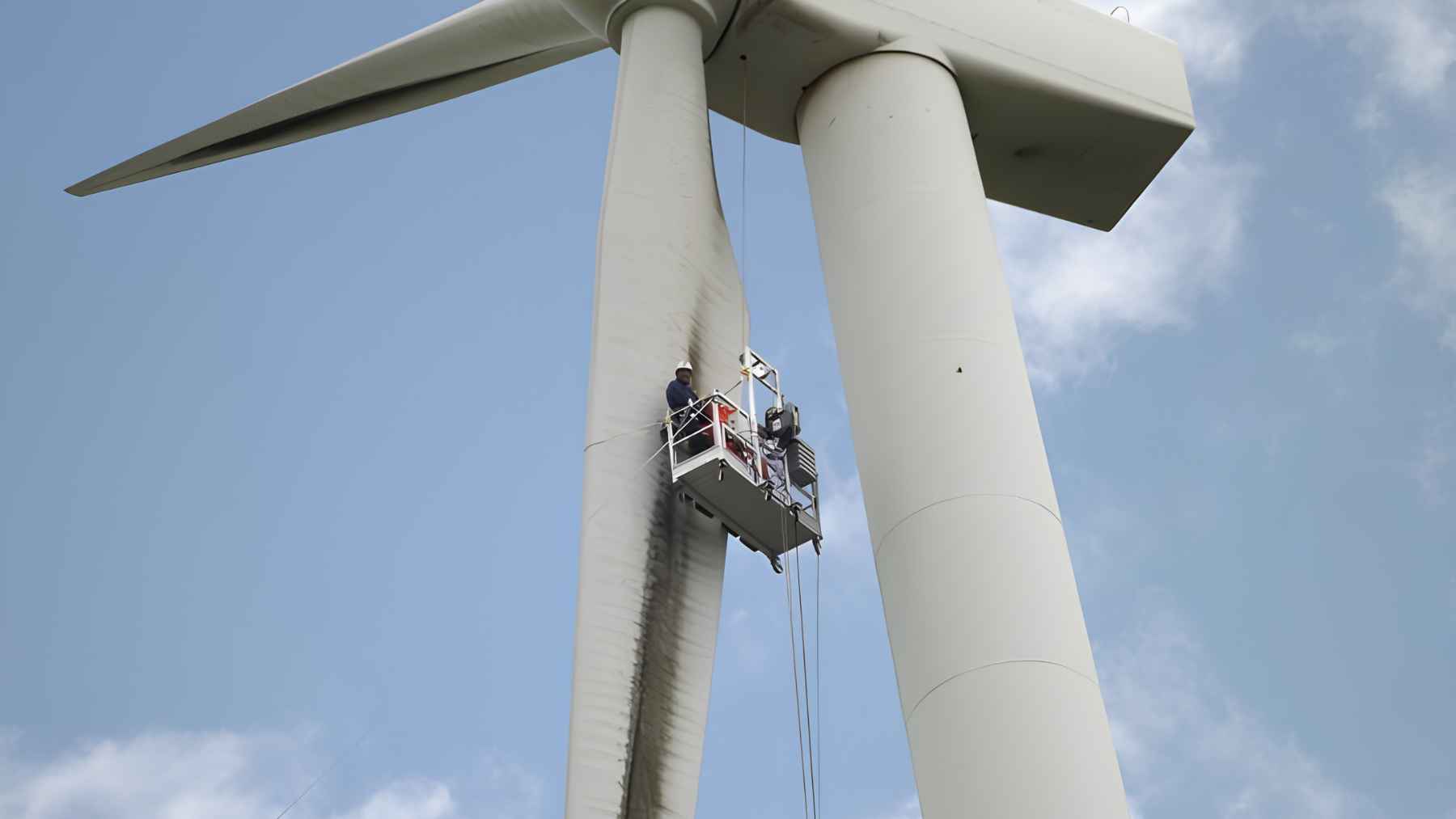 Technicians inspecting a contaminated wind turbine blade from a suspended platform.