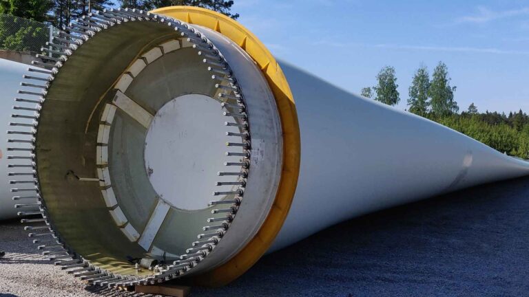 Large wind turbine blade lying on the ground with its composite structure exposed.