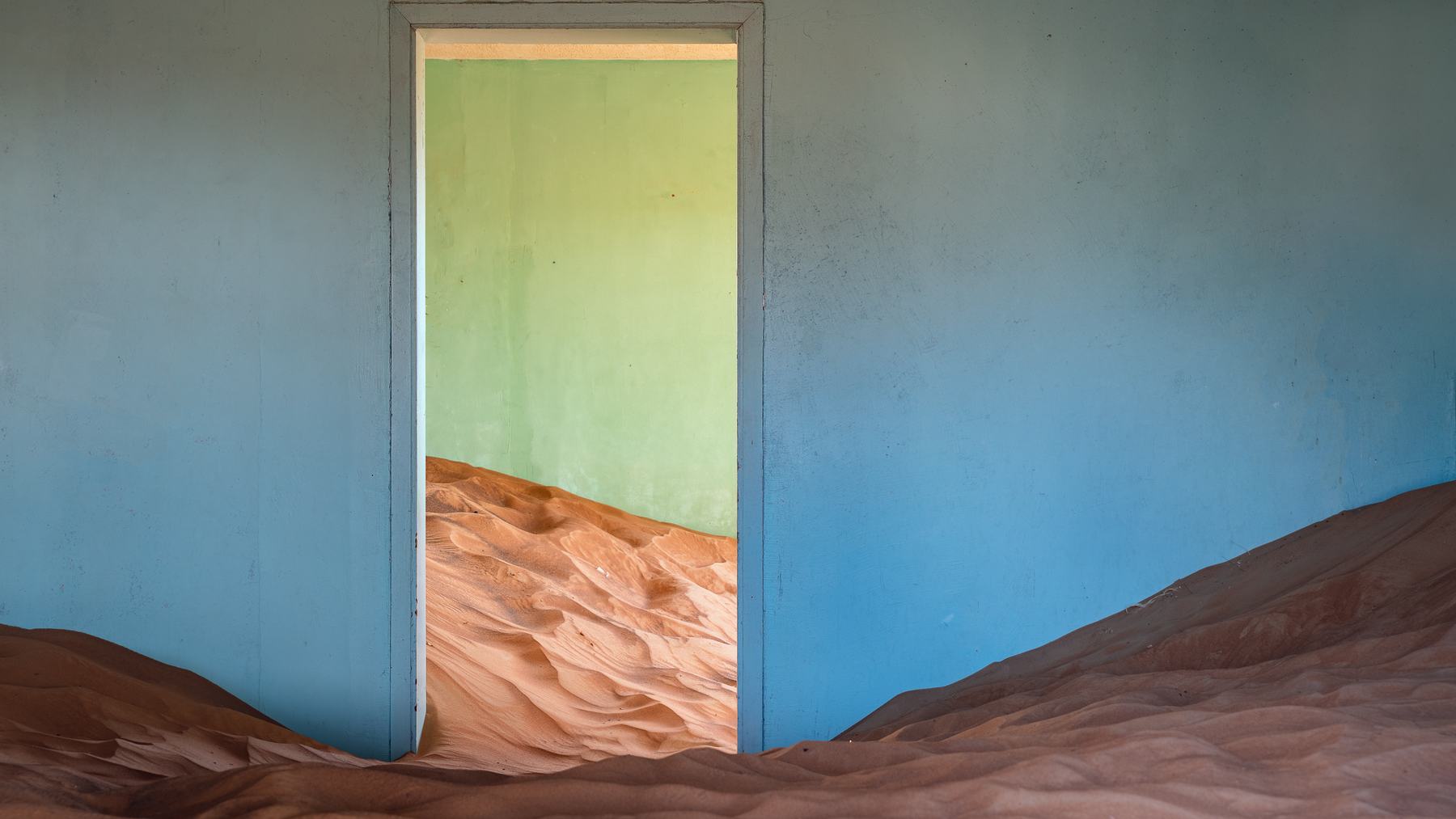 Sand drifts filling a blue-walled room and doorway in the Al Madam ghost village in Sharjah, UAE