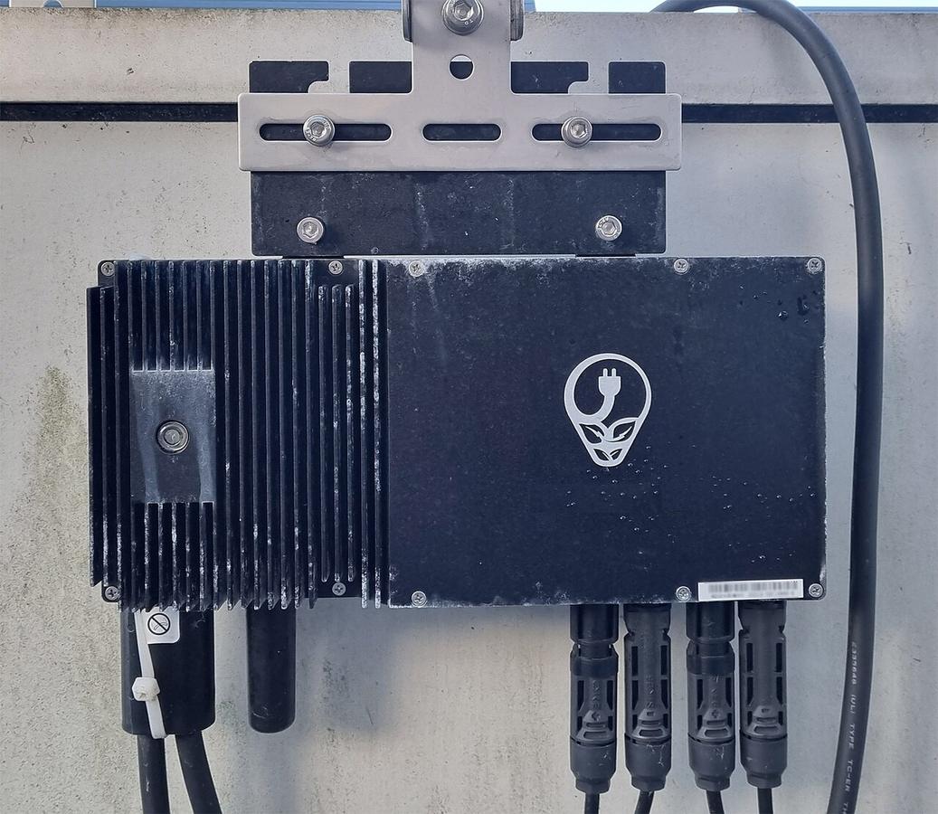 Micro-inverter of a balcony solar system mounted behind a panel, with its cables and connectors