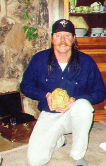 Barry Clay kneels holding a large gold nugget
