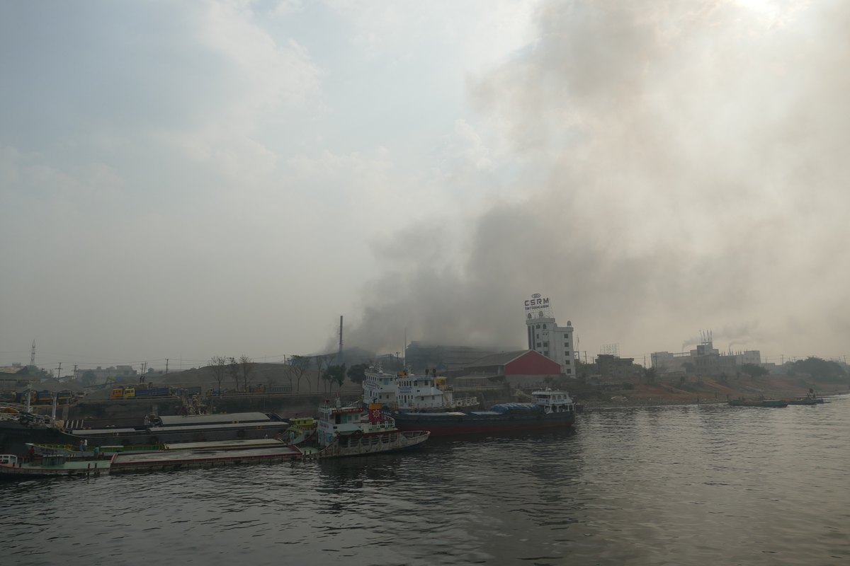 Smoke rising over boats moored on the Buriganga River near Dhaka
