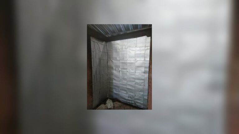 Tetra Pak cartons stapled into shiny panels lining two walls of a test corner under a corrugated metal roof
