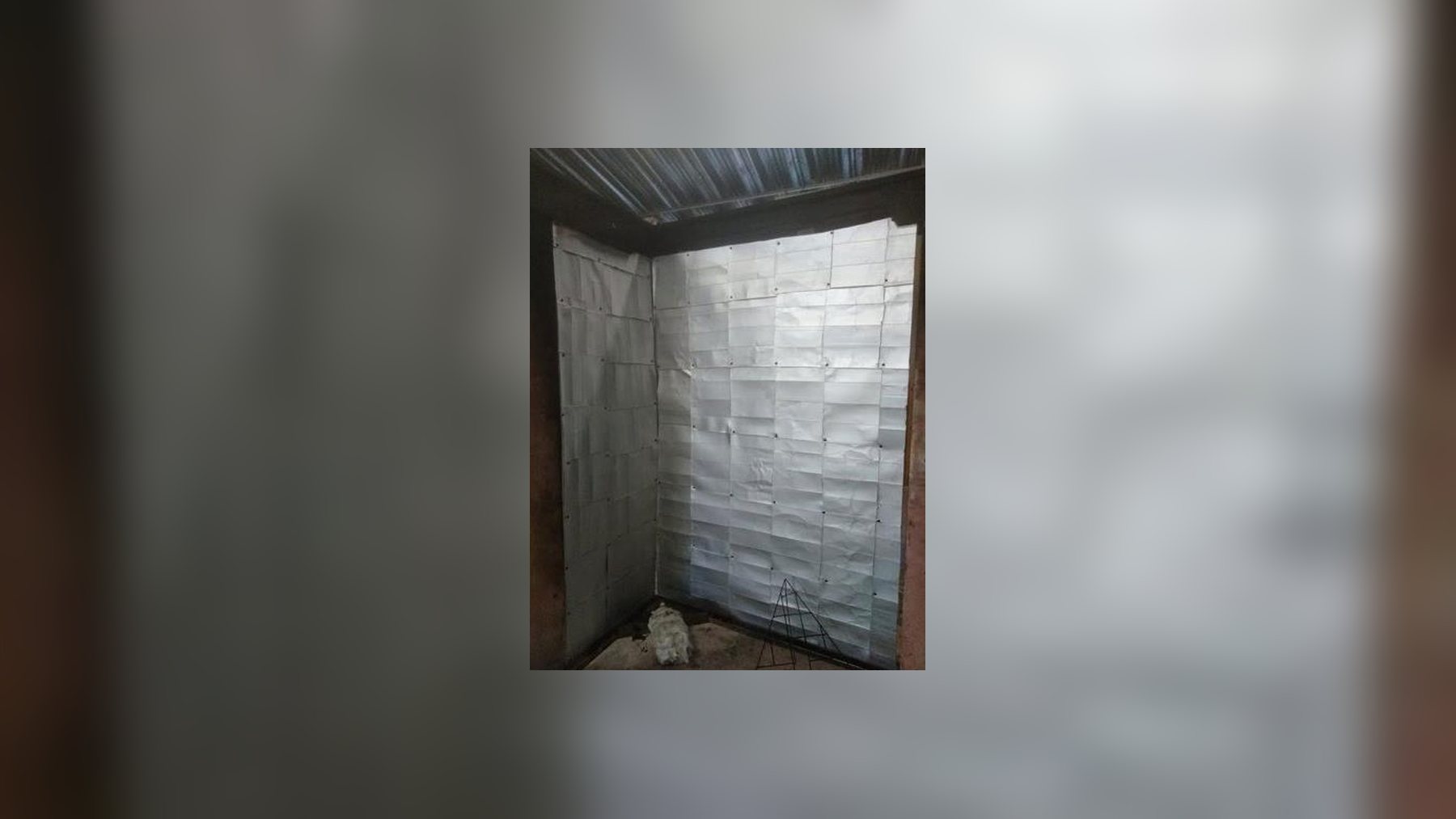 Tetra Pak cartons stapled into shiny panels lining two walls of a test corner under a corrugated metal roof