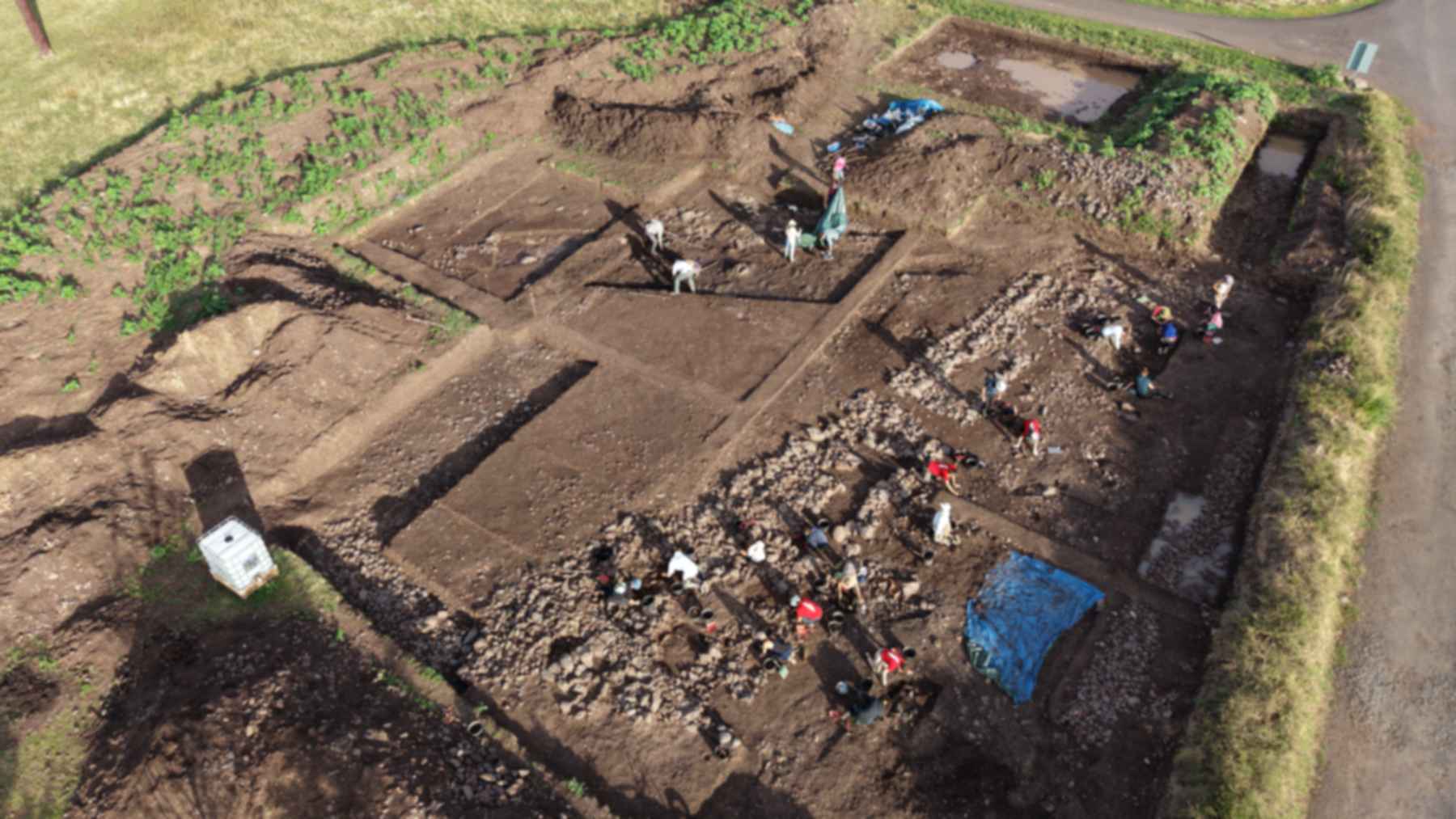 Drone view of the 2026 excavation of the Gallic mint at Corent, France, with stone foundations and diggers at work