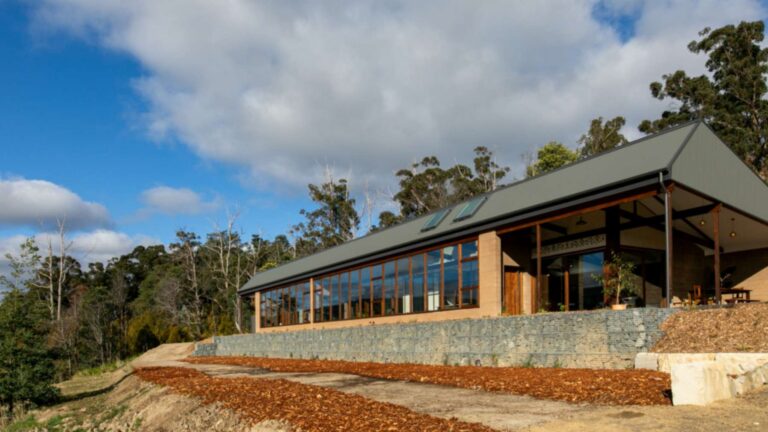 Cygnet Earthship in Tasmania with rammed earth walls, a long north-facing glass sunroom and a rock gabion wall below