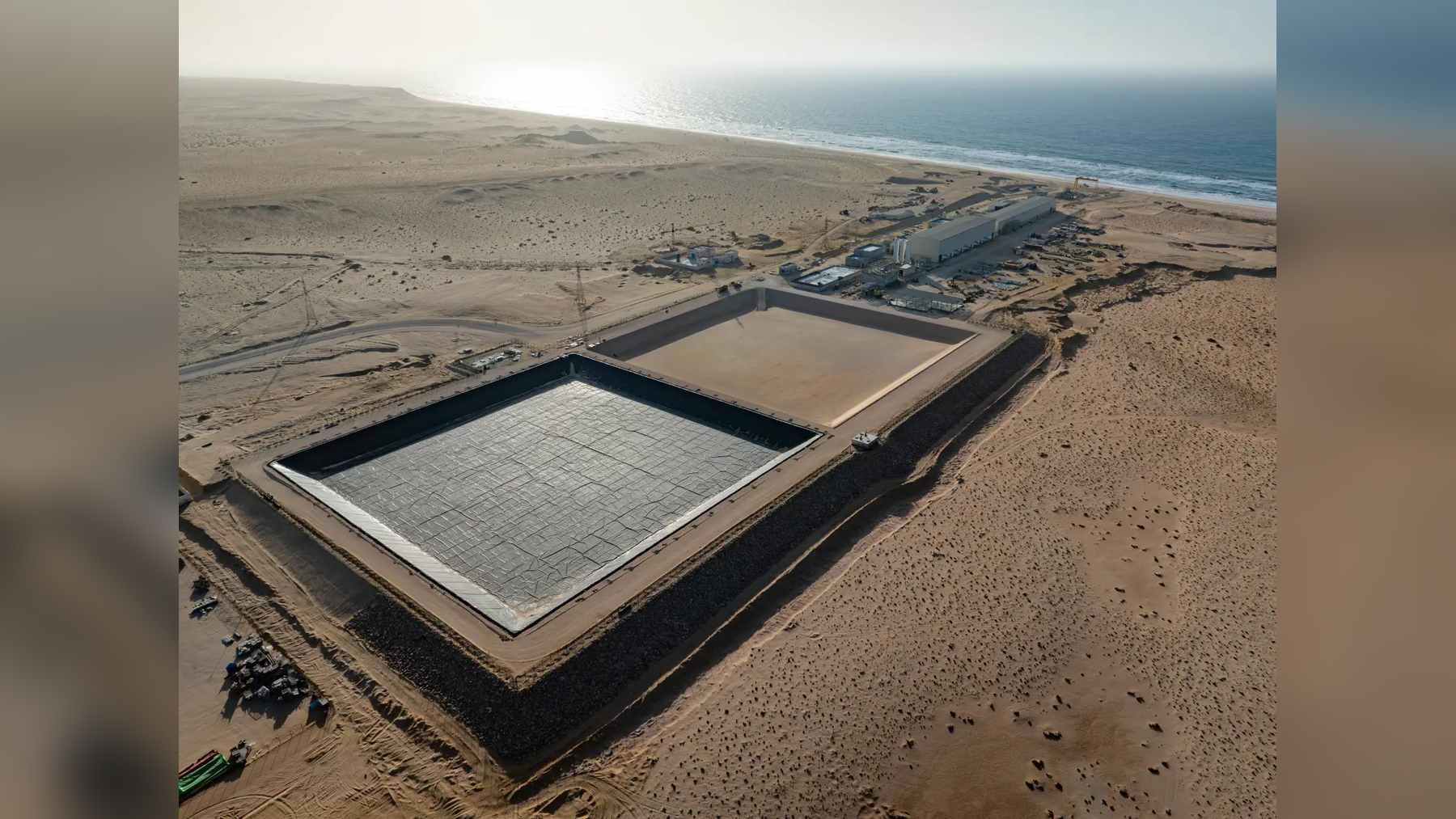 Aerial view of the Dakhla plant site that will produce desalinated Atlantic seawater, with lined basins, buildings and the ocean shore